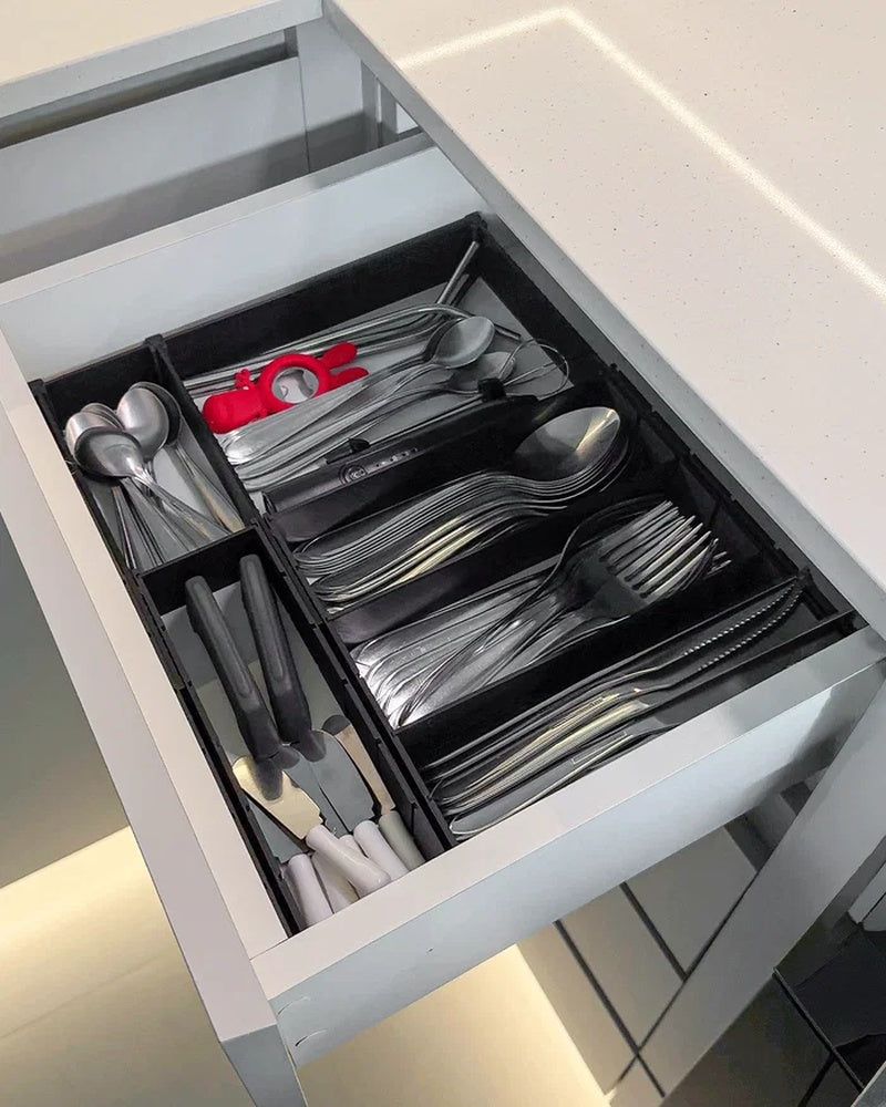 Black drawer organizer inside a kitchen drawer filled with assorted utensils