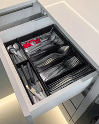Black drawer organizer inside a kitchen drawer filled with assorted utensils