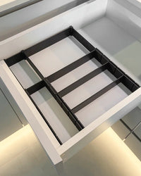 Black partitioned drawer organizer inside an empty white kitchen drawer