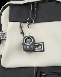 Small grey cat figure in a backpack-shaped frame hanging from a ring and chain on a bag