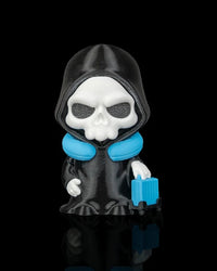 Hooded skull figurine in a black robe with a blue neck pillow and blue suitcase on a black background
