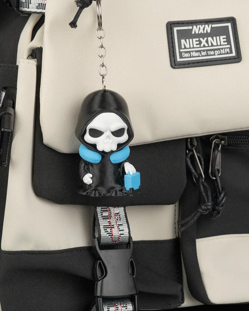 Small hooded skull charm with a metal ring and chain hanging from a beige and black bag