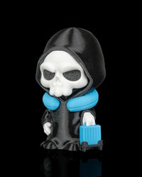 Side view of a hooded skull figurine with a blue neck pillow and blue suitcase on a black background