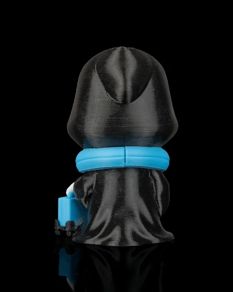 Back view of a black hooded figurine with a blue neck pillow and small suitcase visible at the side