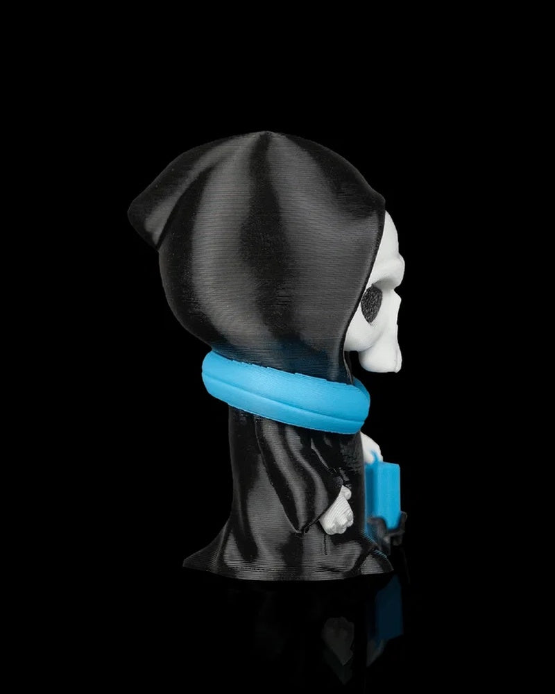 Profile view of a hooded skull figurine in a black robe with a blue neck pillow on a black background