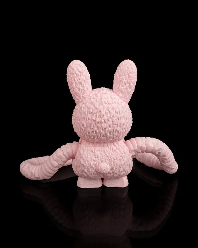 Back view of a pink monster figurine with tall ears and long arms on a black background