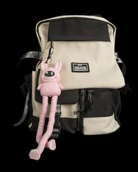 Pink one-eyed monster figure hanging from a beige and black backpack