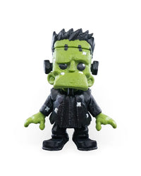 Front view of a green monster figurine with black hair, black clothing, neck bolts, and white patches on a white background.