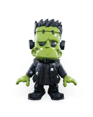 Front view of a green monster figurine with black hair, black clothing, neck bolts, and white patches on a white background.