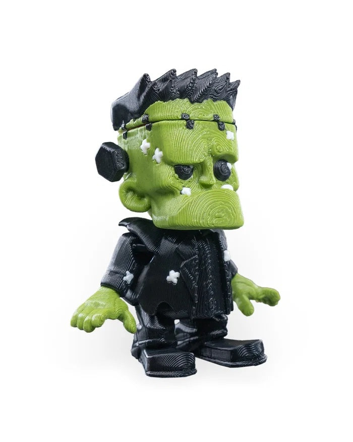 Angled front view of a green monster figurine with black spiky hair, black outfit, and white patches on its face and jacket.