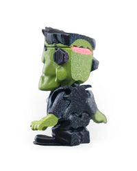 Left side view of a green monster figurine with black flat hair, neck bolt, black outfit, and pink detail at the back of the head.