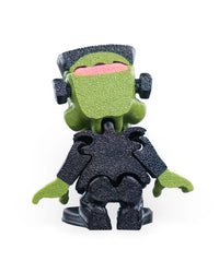Rear view of a green monster figurine with black hair, neck bolts, textured black clothing, green hands, and a pink head detail.