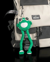Green frog figure with long legs hanging from a metal ring and chain on a backpack