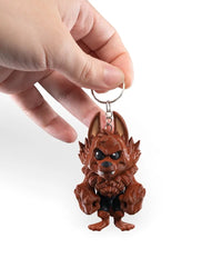A hand holding a metal ring attached to a reddish-brown monster figure with tall ears, black eyes, fangs, and large hands.