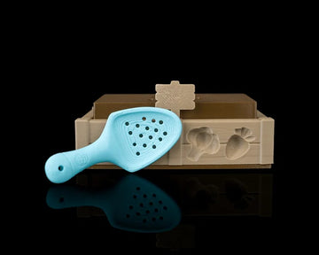 Tan garden bed tray with a brown insert, small sign, and blue perforated shovel on a black background.
