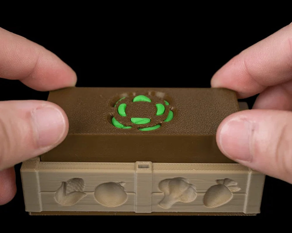 Hands press a brown rectangular insert over a green shape inside a tan garden bed tray.