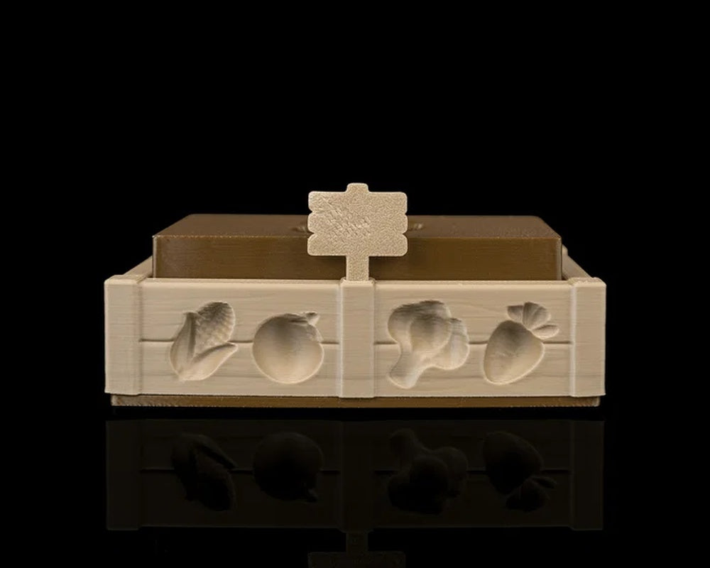 Front view of a tan garden bed tray with raised vegetable shapes, brown insert, and small sign.