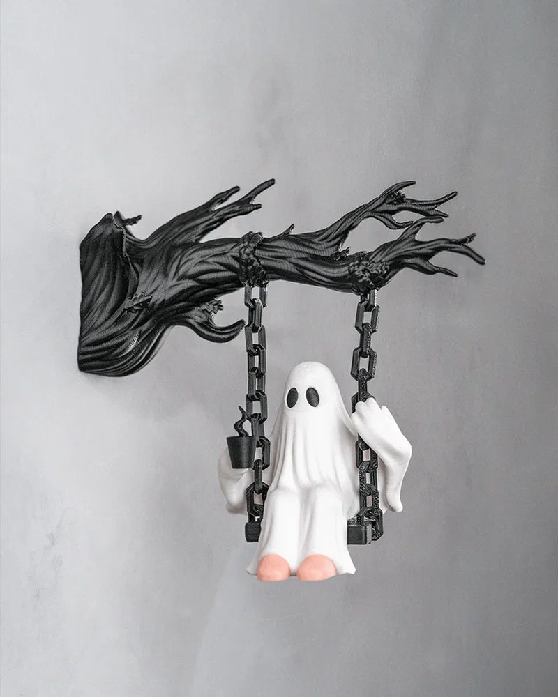 White ghost figurine seated on a black swing hanging from a dark branch-like support against a gray wall