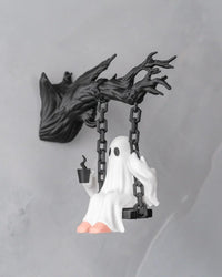 Angled view of a white ghost figurine on a black swing holding a small dark cup-like object
