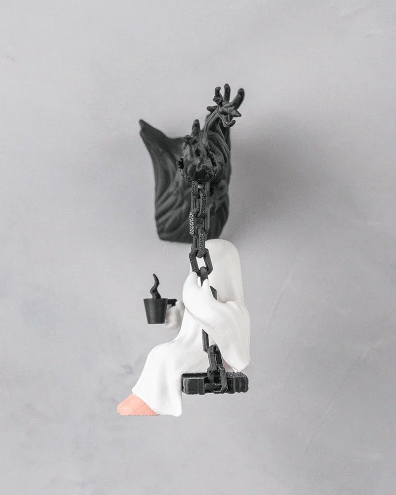 Side view of a white ghost figurine seated on a black swing with chain-like supports