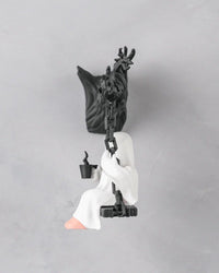 Side view of a white ghost figurine seated on a black swing with chain-like supports