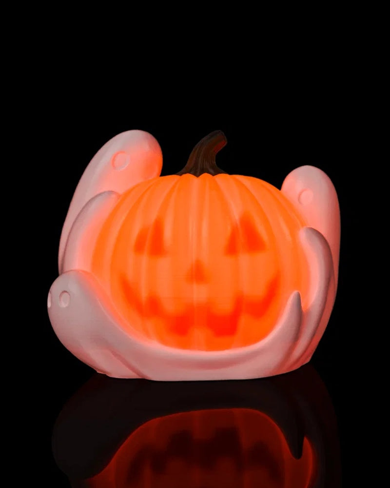 Glowing orange pumpkin lamp with white ghost shapes on a black reflective surface.