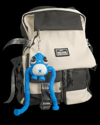 Blue monster figure hanging from a ring and chain on a cream and black backpack