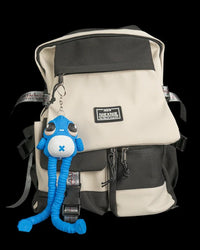 Blue monster figure hanging from a ring and chain on a cream and black backpack with long legs dangling