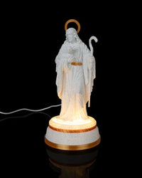 White shepherd statue with gold halo and staff on a lit round base against a black background, with a cord visible to the side.