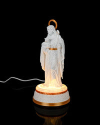 Angled view of a white shepherd statue with gold halo and staff on a glowing round base against a black background.