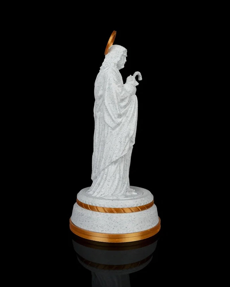 Side view of a white robed shepherd statue holding a staff on a gold-accented round base against a black background.