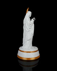 Side view of a white robed shepherd statue holding a staff on a gold-accented round base against a black background.