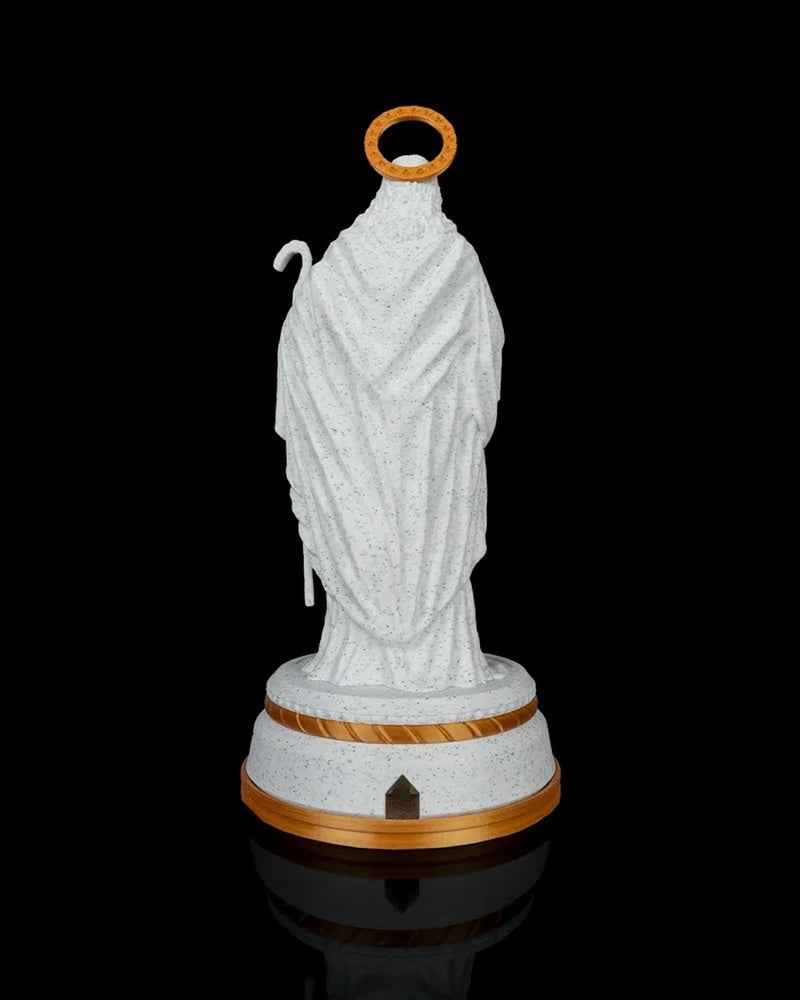 Back view of a white robed shepherd statue with a gold halo on a round base against a black background.