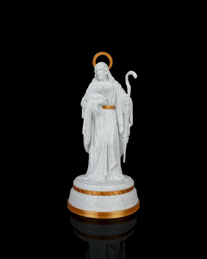 Front view of a white shepherd statue with gold halo, staff, and gold-accented round base against a black background.
