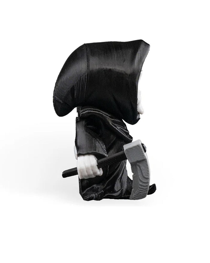 Side view of a hooded skull figure in a black robe holding a gray blade-like prop at its side.