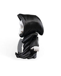 Side view of a black hooded skull figure with a gray blade-like prop against a white background.