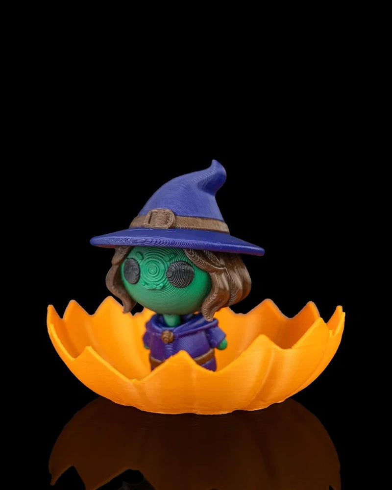 Angled view of a small witch character with a blue hat and green face in an orange pumpkin shell