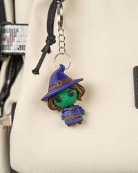 Small witch character hanging from a metal ring and chain against a light fabric surface