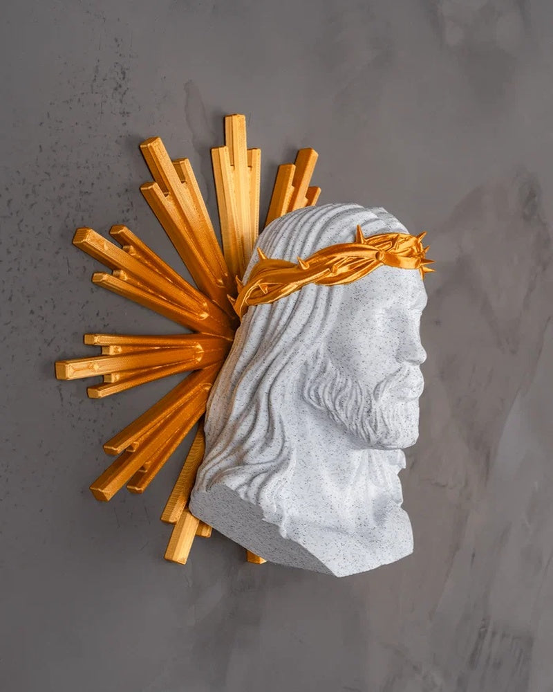 Side view of a white Christ bust with a gold crown and radiating halo on a gray surface