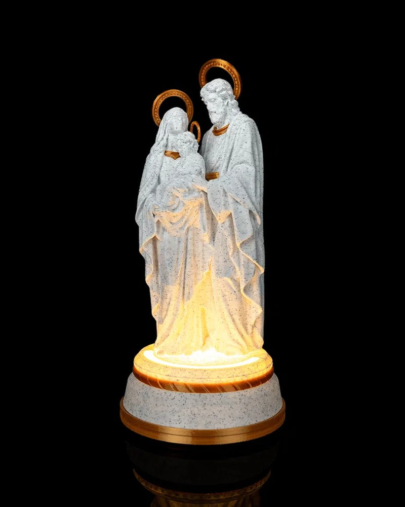 White speckled statue of three robed haloed figures on a round base glowing warmly against a black background.