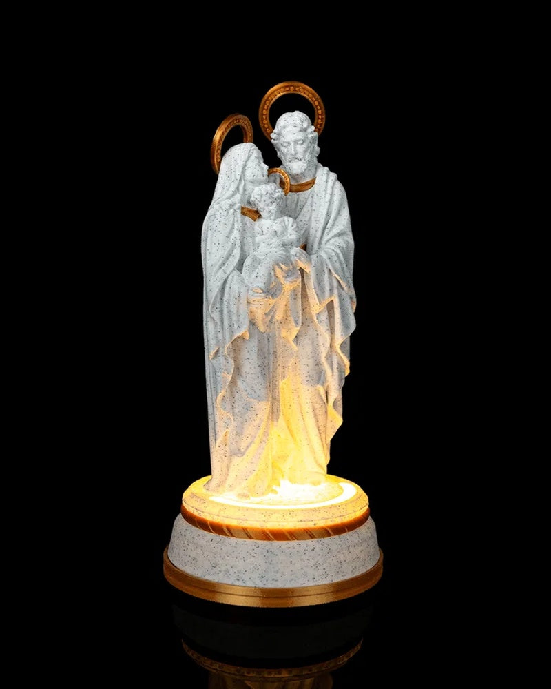 Front view of a white speckled robed group statue with gold halos and a bright illuminated base.
