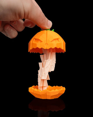 Hand holding an orange jack-o'-lantern pumpkin object with the top raised and a pale twisted center visible on a black background