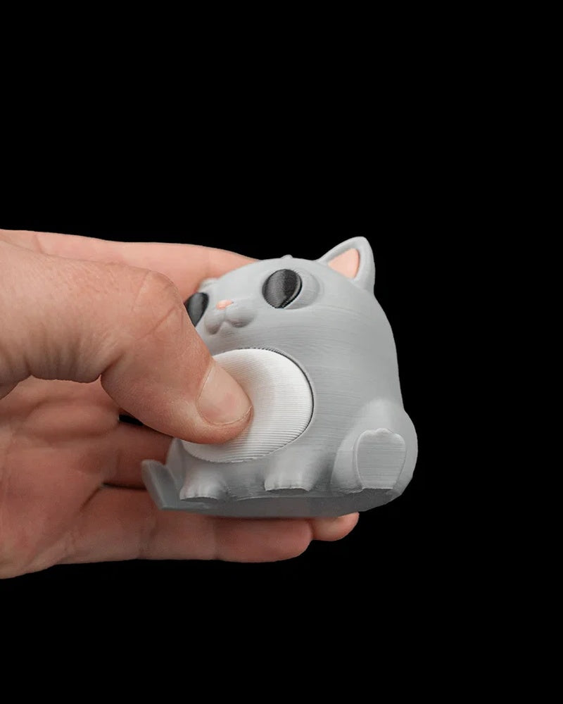 A hand holding a gray cat figure with dark eyes, pink ears, and a white belly.