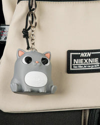 Gray cat figure hanging from a visible metal ring and chain on a beige bag.