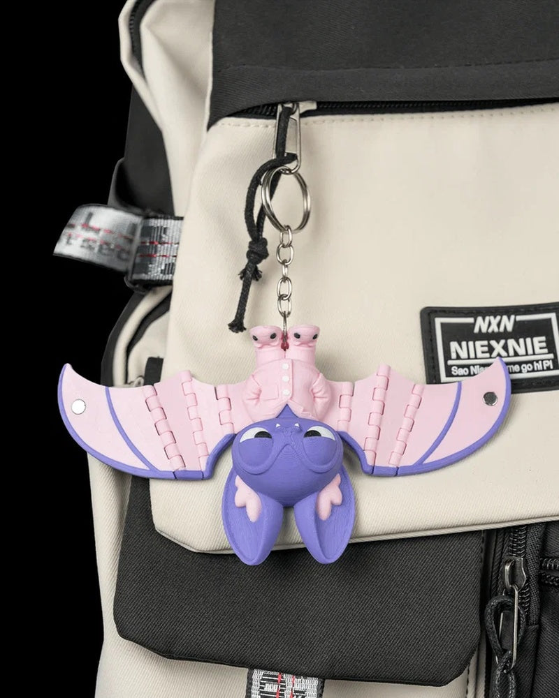 Purple and pink bat figure hanging from a ring and chain on a bag