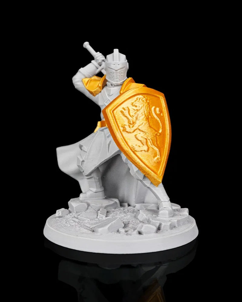 Gray knight figurine with gold shield and shoulder armor holding a raised sword on a round rocky base