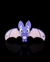Purple and pink bat figurine with wide open wings on a black background