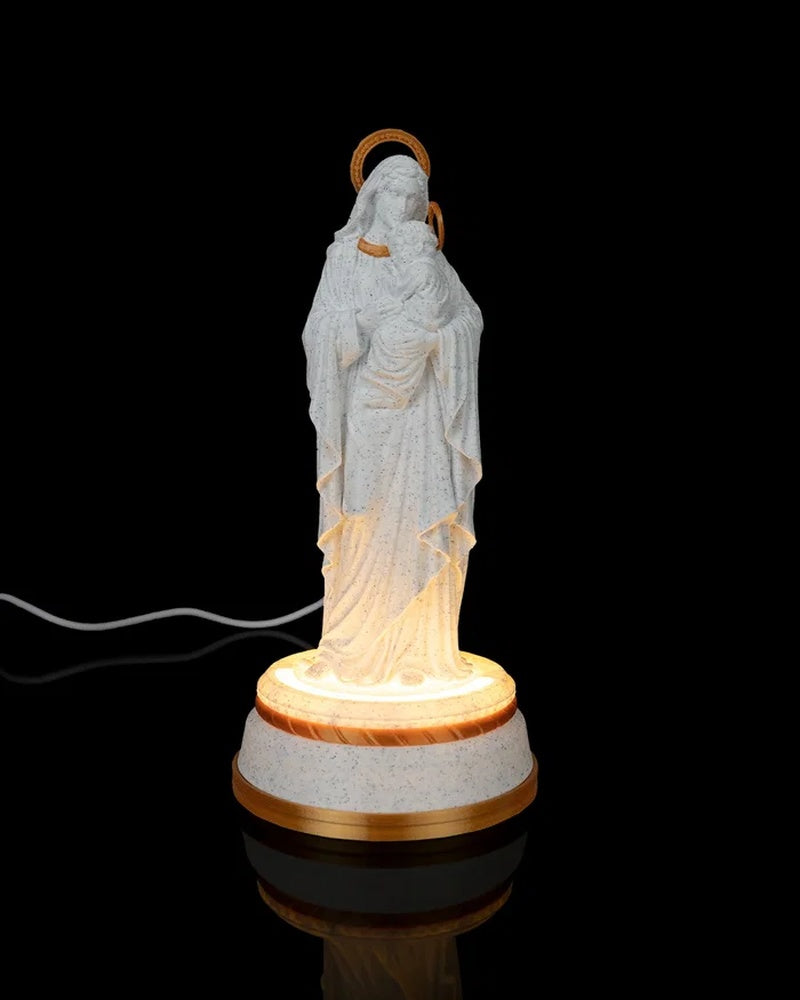 Mary holding Jesus statue on a glowing round base against a black background with a cord visible behind it