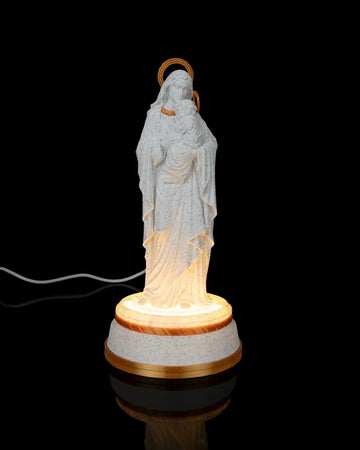 Mary holding Jesus statue on a glowing round base against a black background with a cord visible behind it