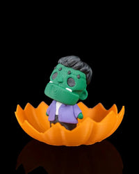 Angled view of a green monster figurine in an orange jagged pumpkin shell on a black background